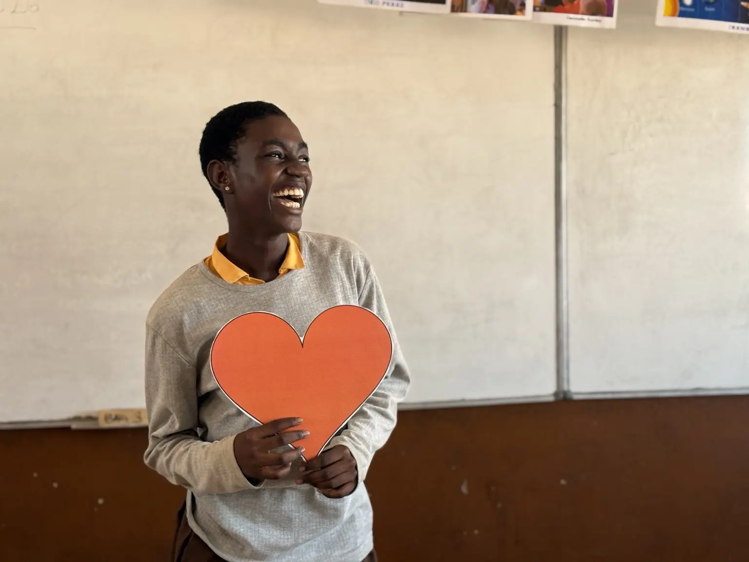 A student smiling while holding a heart during an Ayola classroom activity.